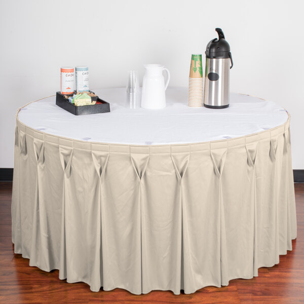 A table with a Snap Drape bone table skirt, white tablecloth, and a tray of drinks.