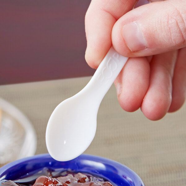 A person holding a white Eco-Products compostable plastic spoon over a bowl of jam.