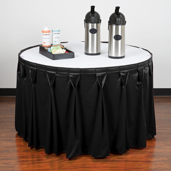 A table with a black Snap Drape Wyndham table skirt and two containers on it.