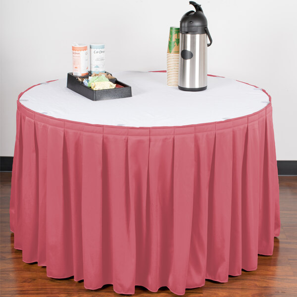 A table skirt with a dusty rose color on a table with a red tablecloth and a tray of food on it.