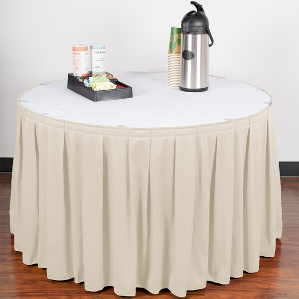 A table with a Snap Drape Wyndham bone box pleat table skirt on it with a tray of coffee cups.