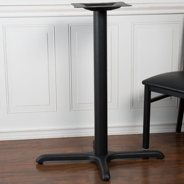 A sand black stamped steel BFM Seating counter height table base with a black chair in front of it.