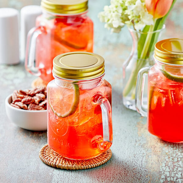 A group of Acopa Rustic Charm mason jars filled with red drinks and lime slices on a counter.