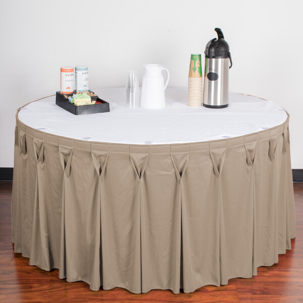 A table with a beige Snap Drape Wyndham table skirt on a table with a white tablecloth and a tray of drinks.