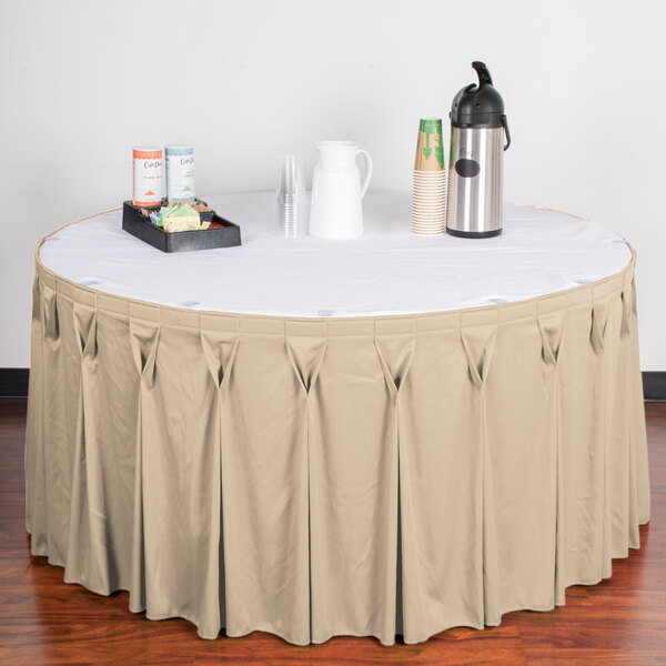 A table with a white tablecloth and a tray of drinks on a table with a Snap Drape Wyndham cream table skirt.