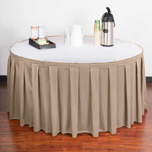 A table with a beige box pleat table skirt on a table with a tray of drinks.