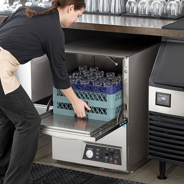 A woman in a black apron putting glasses in a Noble Warewashing undercounter dishwasher.