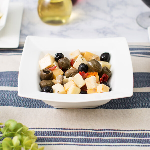 A bowl of cheese and olives on a table.