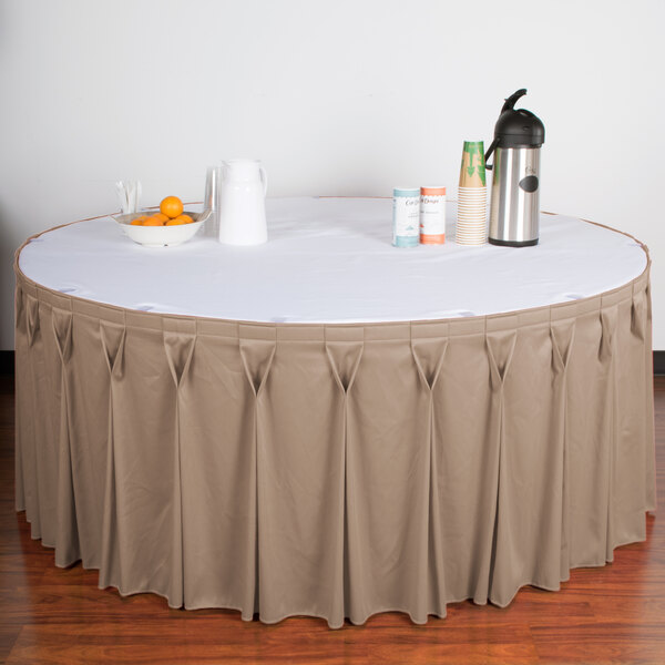A table with a beige Wyndham table skirt with a bow tie pleat on it.