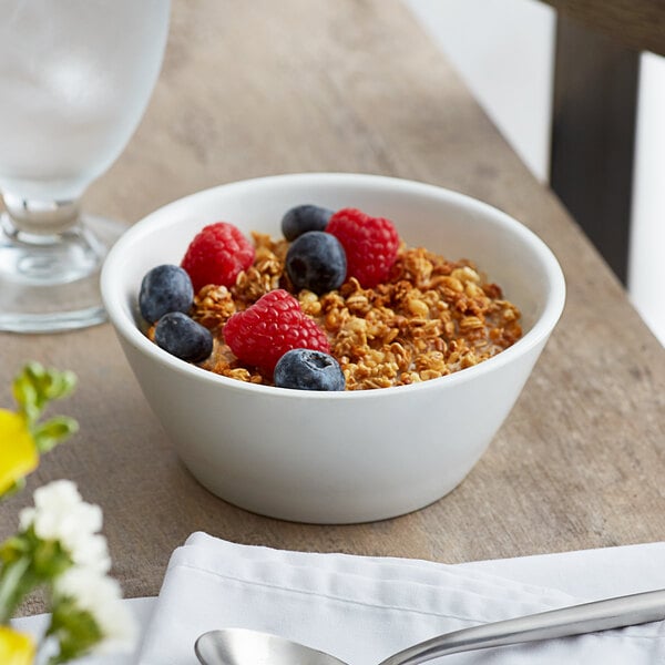 A bowl of cereal with raspberries and blueberries on a table.