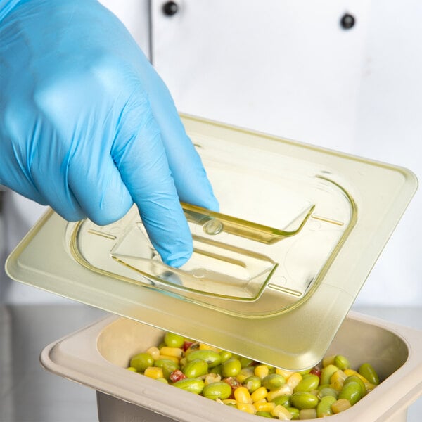 A gloved hand using a Cambro amber plastic lid to cover a container of food.