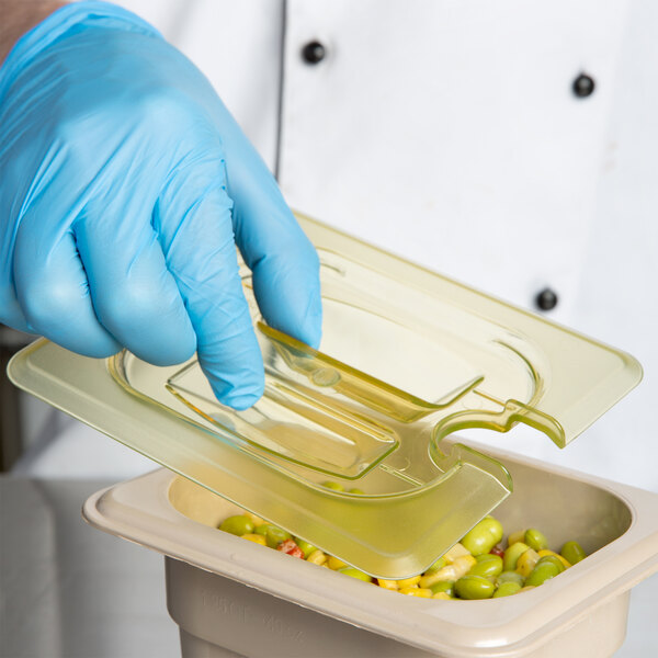 A gloved hand using a Cambro amber plastic lid to cover a container of food.