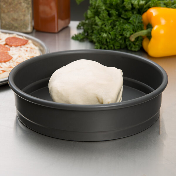 A white ball of pizza dough in a black round cake pan.