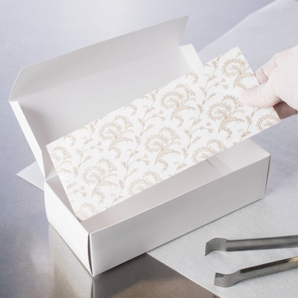 A person using scissors to cut a white 3-ply Glassine pad with a gold floral pattern.