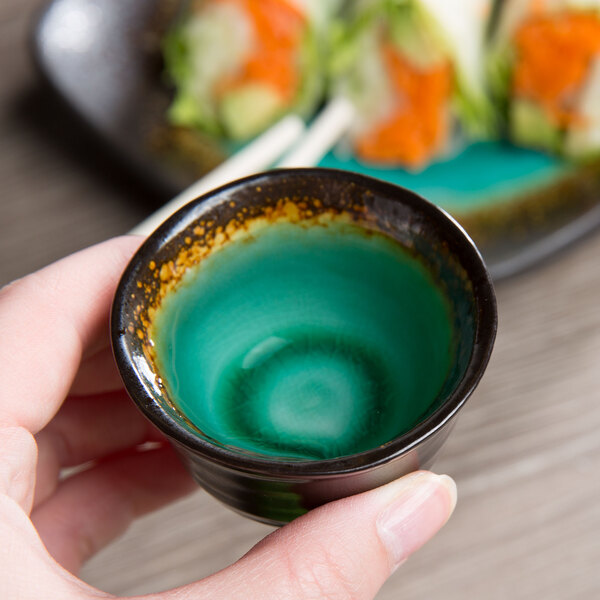 A person holding a small green Libbey stoneware sake cup.