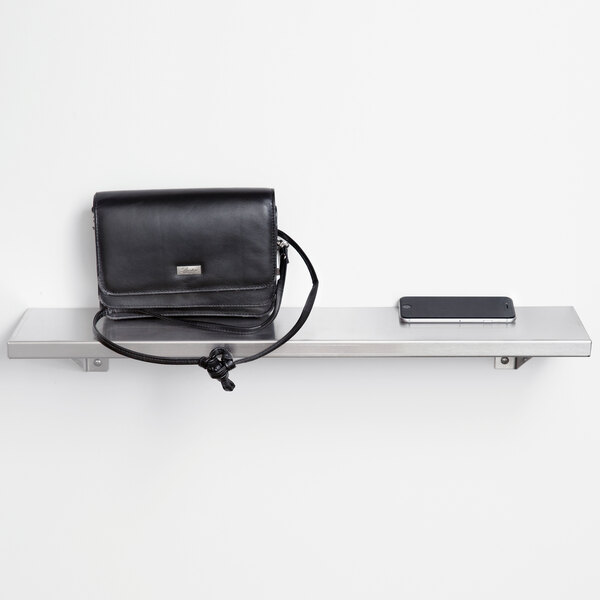 A black purse and a phone on a stainless steel wall shelf.