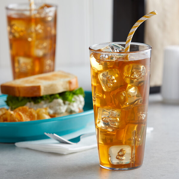 A clear Carlisle polycarbonate tumbler filled with ice tea on a table next to a sandwich.