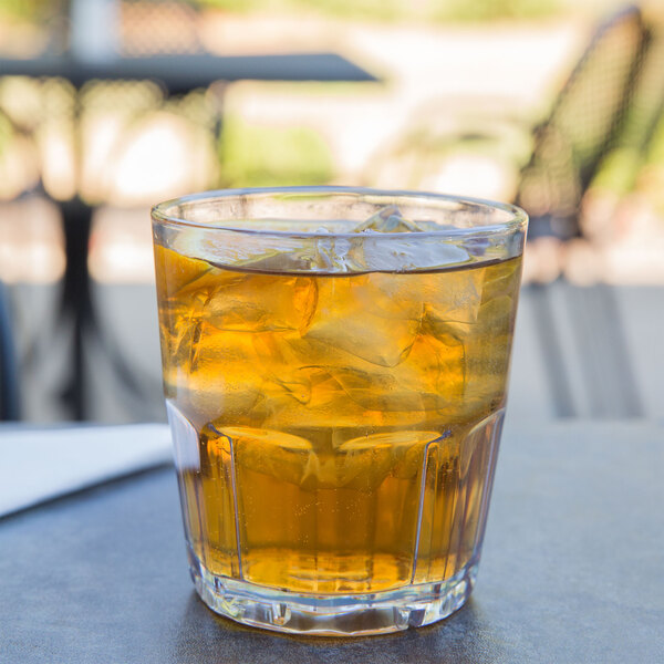 A clear GET Bahama plastic tumbler filled with ice tea on a table outside.