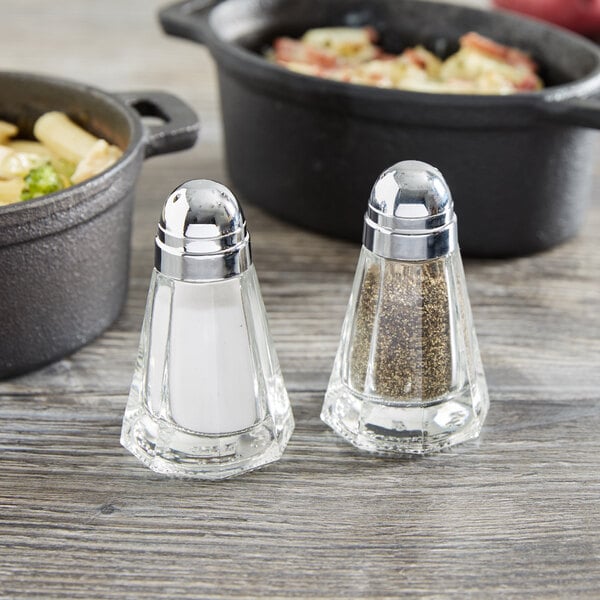 Two Tablecraft glass salt and pepper shakers with chrome plated metal lids on a table.
