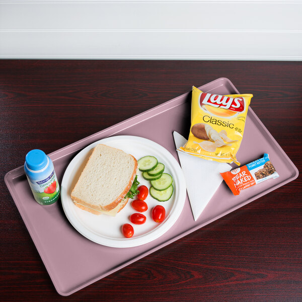A Cambro blush dietary tray with a sandwich, chips, and a drink on it.