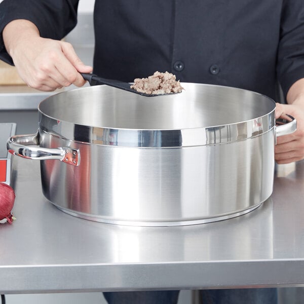 A person stirring food in a Vollrath Centurion brazier pan.