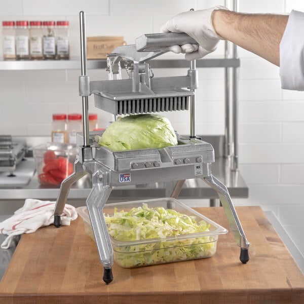 A hand in a glove using a Nemco Easy LettuceKutter to slice lettuce over a clear plastic container.