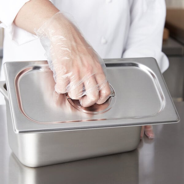 A person wearing plastic gloves holding a Vollrath stainless steel hotel pan cover.
