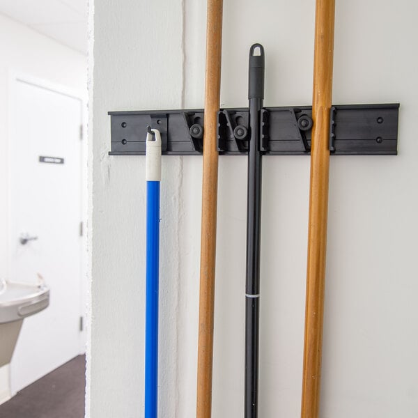 A white Carlisle Roll 'N Grip closet rack with three poles holding brooms.