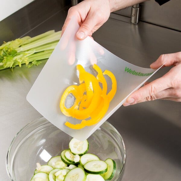A person cutting yellow bell peppers on a white WebstaurantStore flexible cutting board.