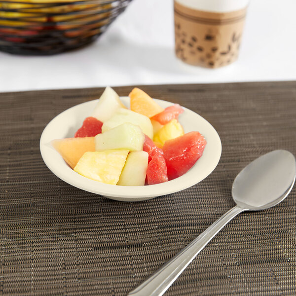 A Carlisle tan melamine fruit bowl with a spoon and a bowl of fruit on a table.