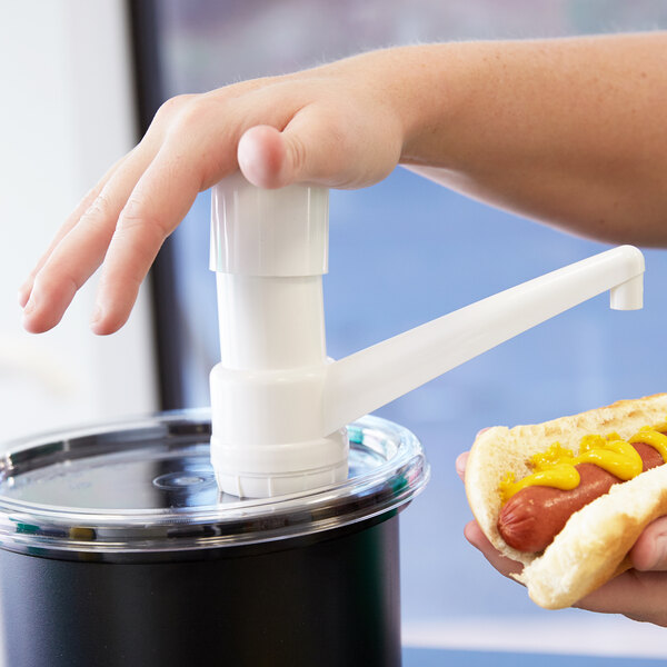 A person using a Cambro clear fixed nozzle pump to dispense mustard onto a hot dog.