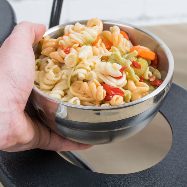 A hand holding a Vollrath stainless steel bowl of pasta with vegetables.