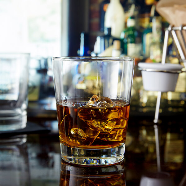 A Libbey rocks glass filled with brown liquid and ice on a bar counter.