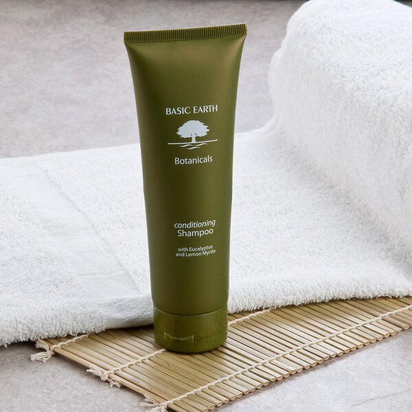 A green bottle of Basic Earth Botanicals Conditioning Shampoo with white text and a flip-top cap on a white towel.