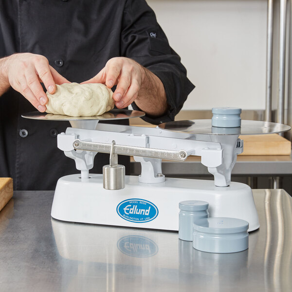 A chef weighing dough on an Edlund stainless steel baker's dough scale.