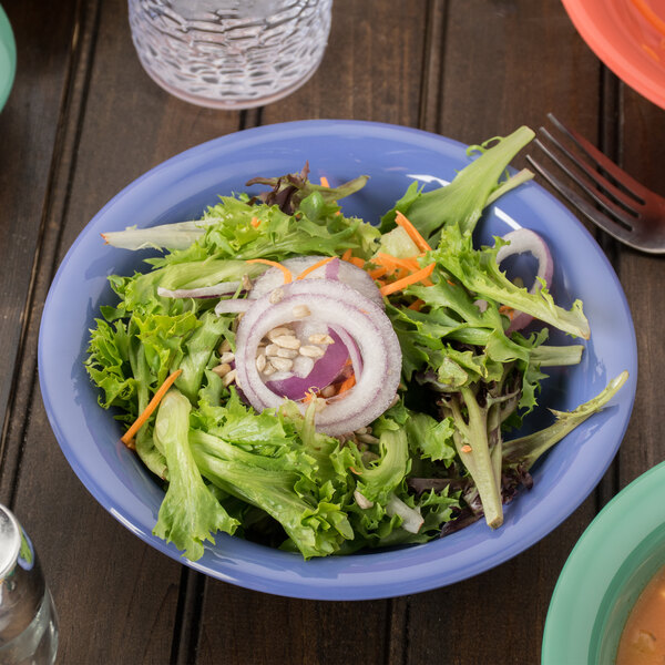A peacock blue melamine bowl filled with salad with onions and carrots.