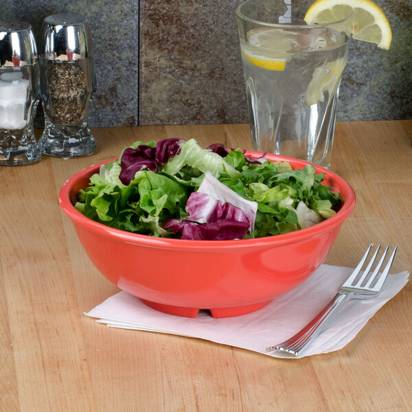 A bowl of salad in a red Thunder Group melamine bowl on a table.