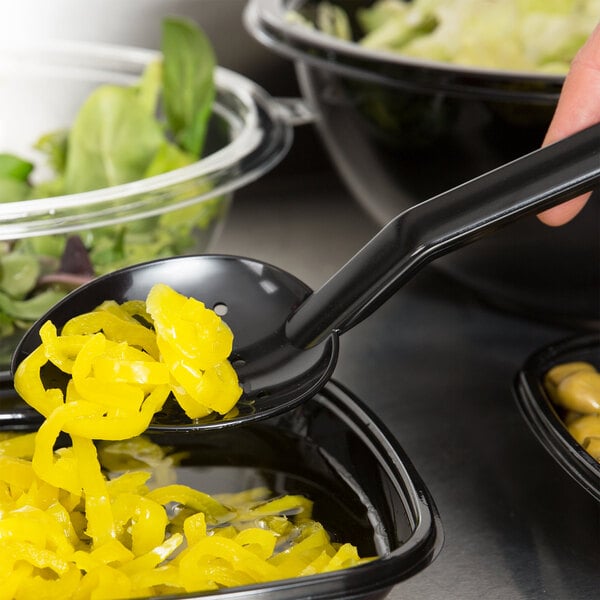 A person using a Thunder Group black perforated salad bar spoon to serve food in a bowl.