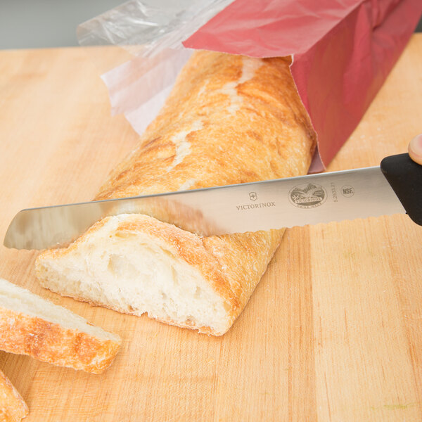 A Victorinox bread knife cutting a loaf of bread on a cutting board.