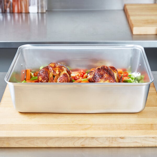 A Vollrath aluminum roaster pan filled with chicken and vegetables on a cutting board.