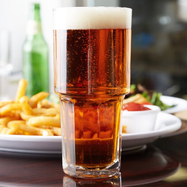 A Libbey Gibraltar stackable cooler glass of beer on a table next to a plate of fries.