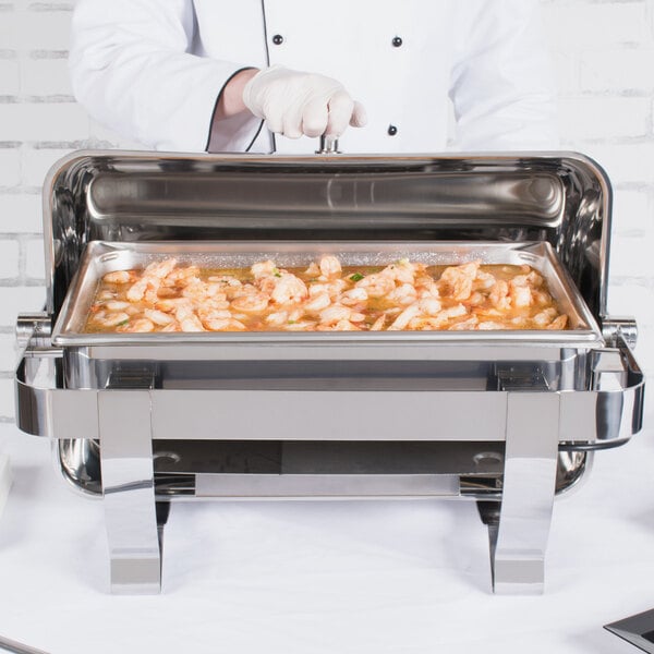 A person in a white glove using a Vollrath Orion electric chafer to serve shrimp on a buffet counter.