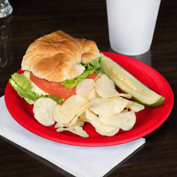 A Carlisle red melamine plate with a croissant sandwich and potato chips on it.