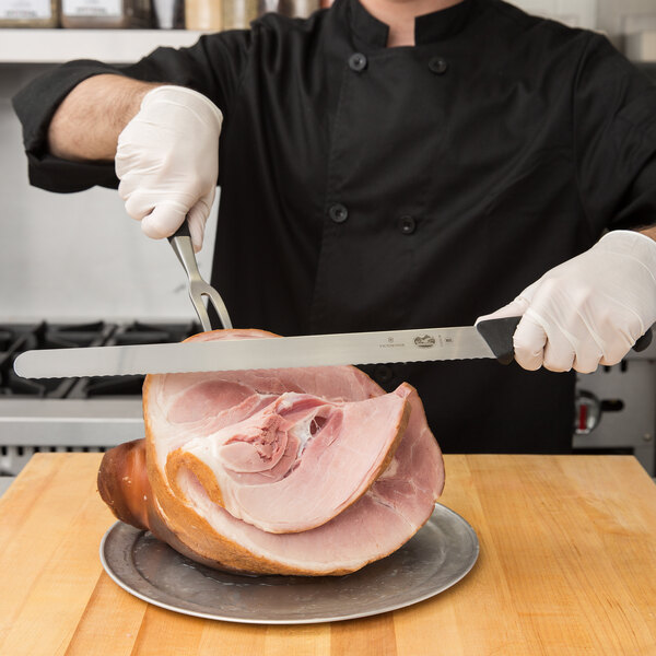 A person in a chef's uniform using a Victorinox wavy edge slicing knife to cut a ham.