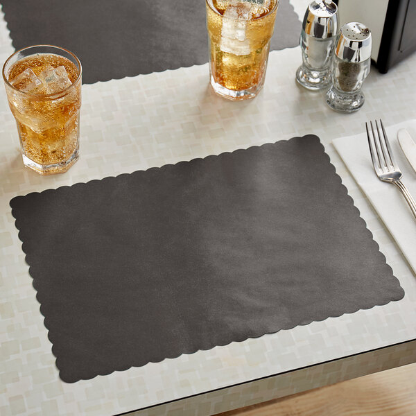 A table set with a Choice black scalloped paper placemat and two glasses of liquid.