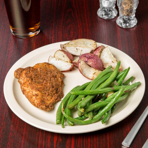 A Carlisle Kingline tan melamine plate with chicken, potatoes, and green beans on a table with a glass of beer.