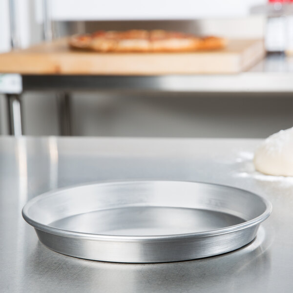 An American Metalcraft aluminum deep dish pizza pan on a counter with a pizza in it.