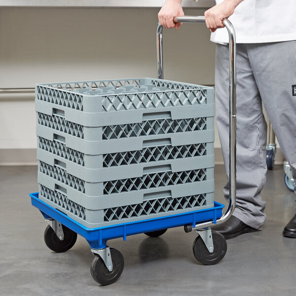 A man pushing a blue Vollrath Traex rack dolly with a stack of crates.