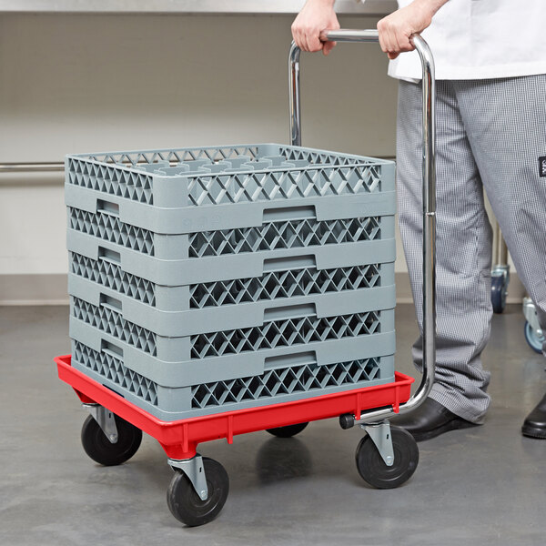 A man pushing a red Vollrath rack dolly with a stack of crates.