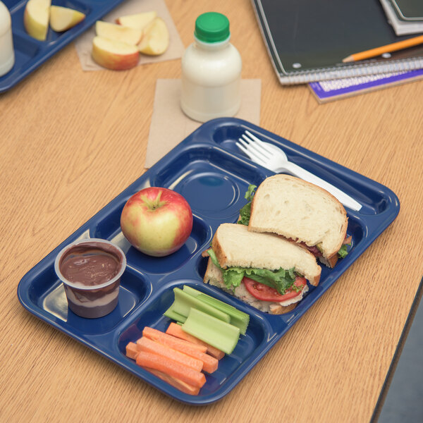 A blue Carlisle 6 compartment tray with sandwiches, fruit, and a cup on a table.